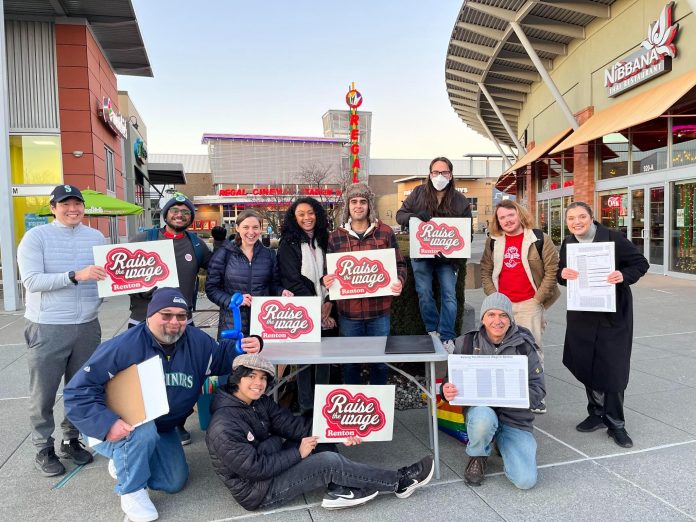 A group of about 15 campaign volunteers hold clip board and campaign signs at a mall plaza.