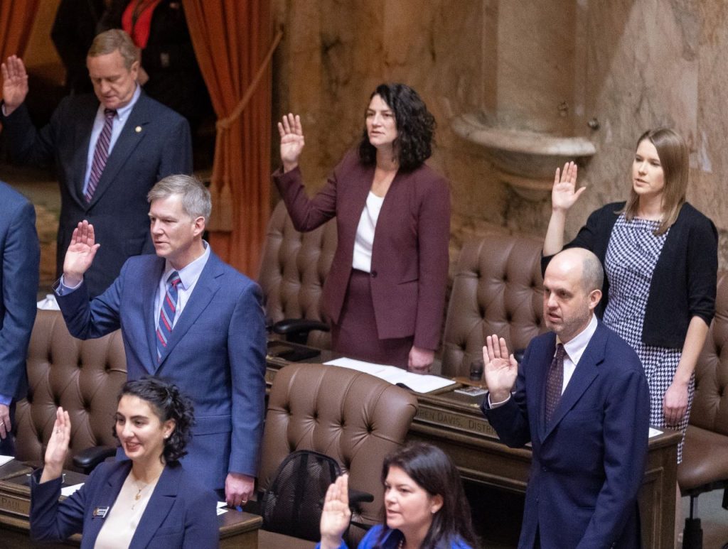 State representatives stand at their desks and raise their right hand to take an oath to start the 2023 session.