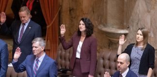 State representatives stand at their desks and raise their right hand to take an oath to start the 2023 session.