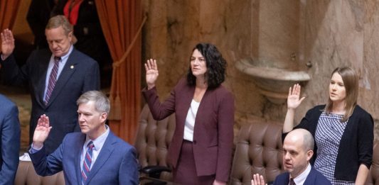 State representatives stand at their desks and raise their right hand to take an oath to start the 2023 session.