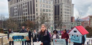 Social housing advocates stand on the steps of Seattle City Hall with their house mascot.