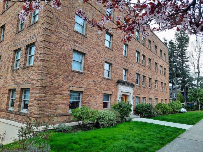 A four-story historic brick apartment building with a blossoming tree out front.