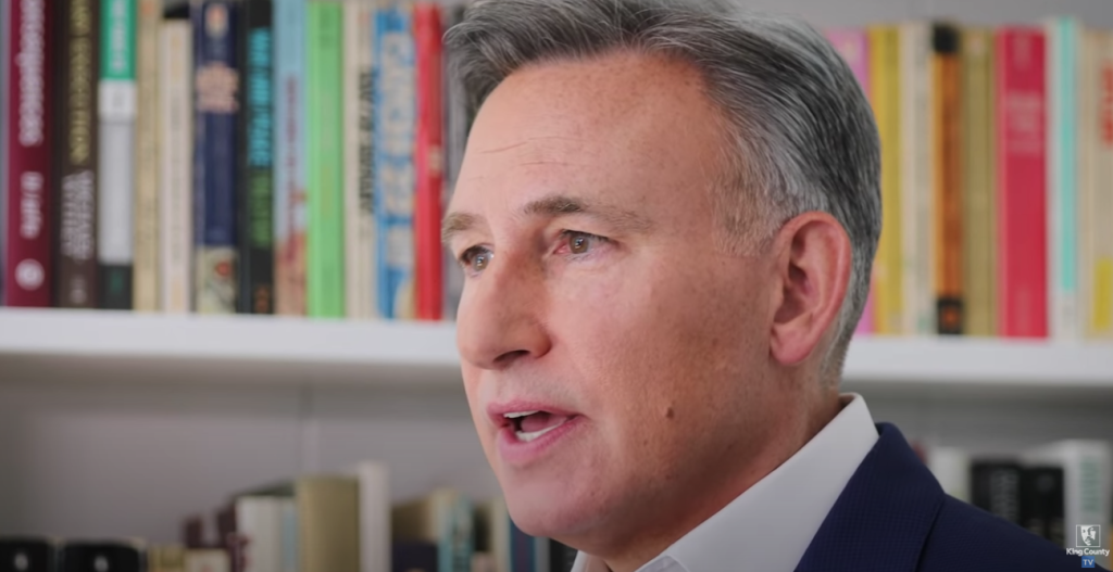 Executive Dow Constantine with books in the background as he gives a speech