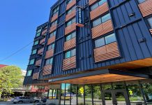 Housing Nonprofits Grapple with Fiscal Crisis and Federal Threats A six-story apartment building with blue metal siding and wood railing for juliette balconies