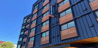 Housing Nonprofits Grapple with Fiscal Crisis and Federal Threats A six-story apartment building with blue metal siding and wood railing for juliette balconies