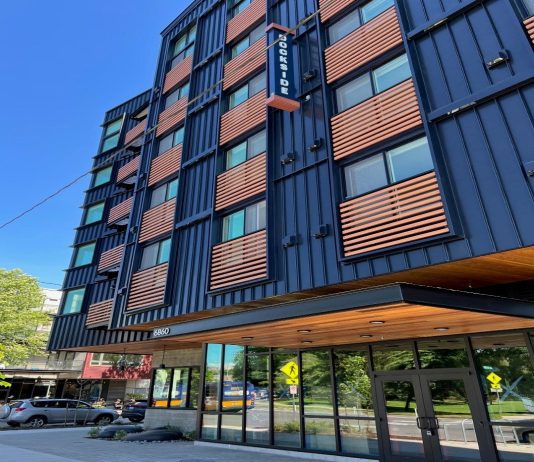 Housing Nonprofits Grapple with Fiscal Crisis and Federal Threats A six-story apartment building with blue metal siding and wood railing for juliette balconies