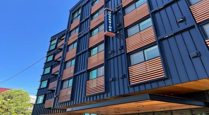 Housing Nonprofits Grapple with Fiscal Crisis and Federal Threats A six-story apartment building with blue metal siding and wood railing for juliette balconies