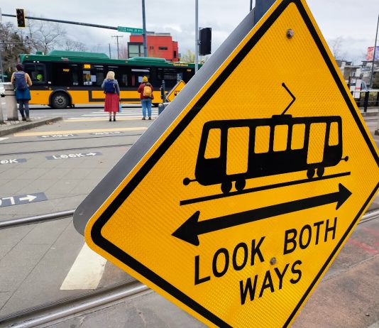 New Energy for Changes on MLK Corridor, But Few New Ideas A look both ways yellow sign includes a light rail symbol. Pedestrian wait at the opposite corners of MLK Way.