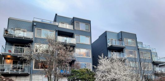 Twin four-story apartments with cherry trees in front.