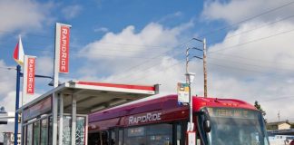 A red and gold RapidRIde bus waits an a bus shelter with the sign indicating it's headed to Federal Way Transit Center.