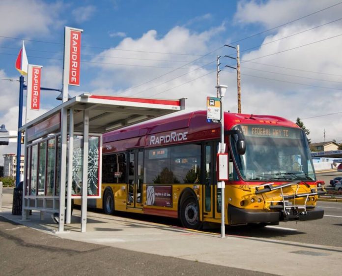 A red and gold RapidRIde bus waits an a bus shelter with the sign indicating it's headed to Federal Way Transit Center.