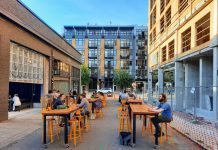 Join The Urbanist for Monthly Meetup on March 21 The back patio at Stoup with Ryan Packer sitting at one of the table and apartment buildings in the background.