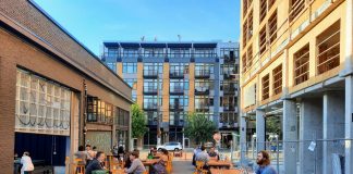 Join The Urbanist for Monthly Meetup on March 21 The back patio at Stoup with Ryan Packer sitting at one of the table and apartment buildings in the background.