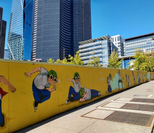 Policy Lab: Will Last Progressive in Seattle Turn On the Lights A fence with a pilot boy cartoon figure surrounding Civic Square with Seattle City Hall and the Columbia Tower skyscraper in the background.