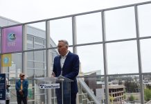 Sound Transit Board Advances Secret ‘Candidate C’ as CEO Pick Constantine wears a suit and stands at a glass lectern in from of the Downtown Bellevue Station plaza overlook of the station platform below.