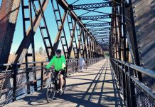 Washington’s Statewide E-bike Rebate Program Is Still on the Way A person bikes on a trestle bridge with a few pedestrians in the background.