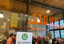 Join The Urbanist for Our Monthly Meetup on May 16 An Urbanist banner standing in a corner of a brewery with a few dozen people gathered chatting.