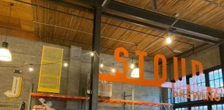 Join The Urbanist for Our Monthly Meetup on April 18 An Urbanist banner standing in a corner of a brewery with a few dozen people gathered chatting.