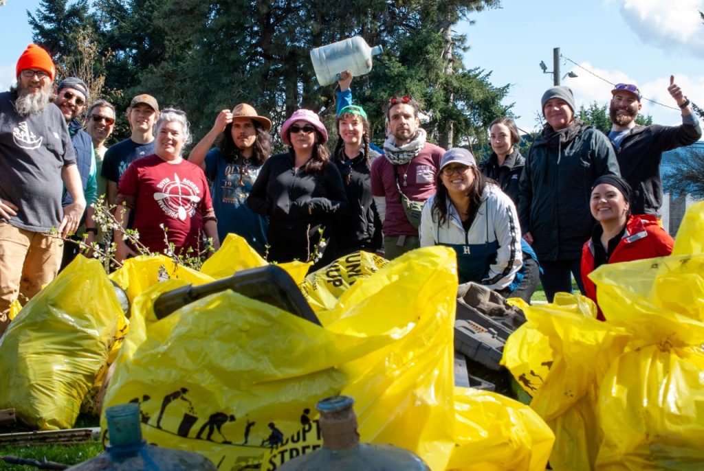 About 15 people pose with big yellow bag of trash pulled from the Duwamish riverbanks