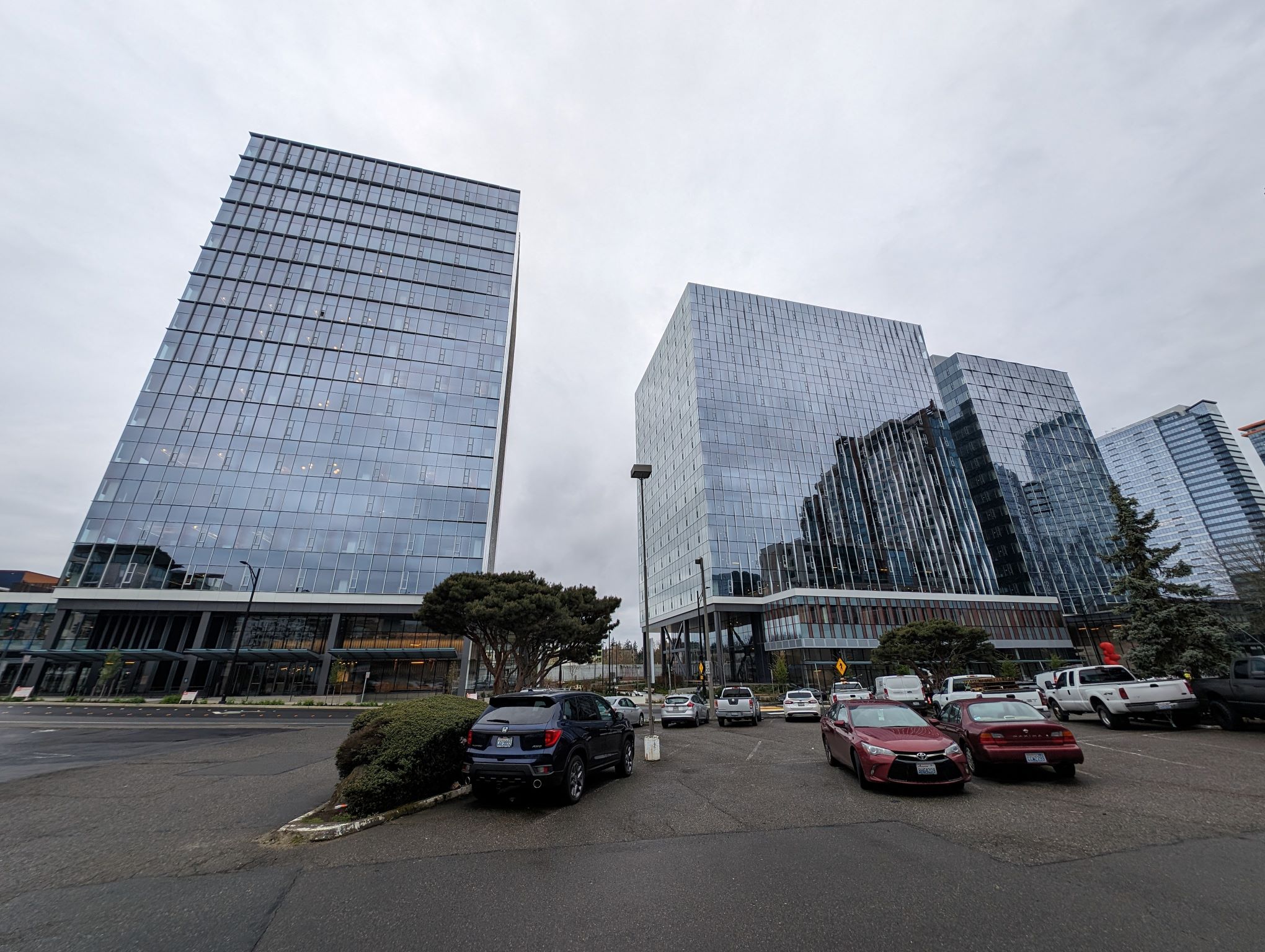 Two shiny glass tower boxes with parking lot in foreground.