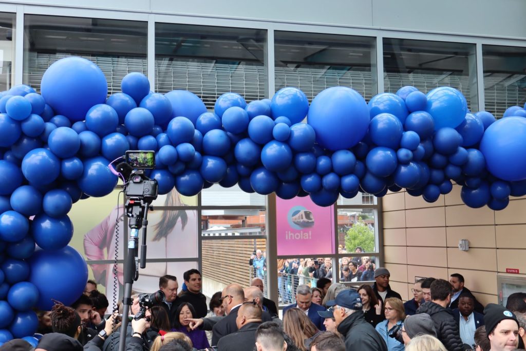 A balloon arch festively marks the Redmond-bound entrance and local officials line up at a ribbon obscured by the crowd of people.