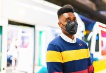 Shaun Scott Aims to Succeed Retiring Rep Chopp as Progressive Champion in Olympia Shaun Scott is a Black man with a hi-top fade and wears an N95 mask while standing in front of a Link light rail train on a station platform.