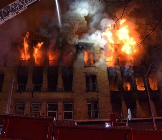 Seattle Aims to Tamp Down Vacant Building Fires Fire and smoke pours out of upper story windows of an old brick building with a fire crane seeking to control them.