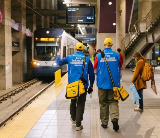 Sound Transit To Launch Platform Fare Inspection in Early June A pair of ambassadors wear blue coats and yellow hats and carry yellow bags.