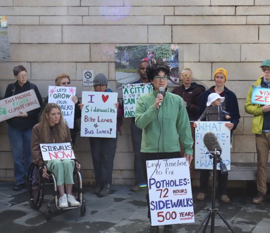 Mobility Advocates Find Support for Bigger Levy in Poll, Council Deliberates Fellow advocates stand behind Cantor and hold signs urging action on safe streets.