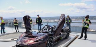 McLaren has its butterfly doors up while a half dozen onlookers in yellow vests take picture or admire the car.