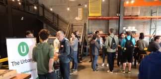 Join The Urbanist for Our Monthly Meetup on July 25th An Urbanist banner standing in a corner of a brewery with a few dozen people gathered chatting.