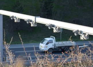 Washington Cities Question Use of License Plate Readers Citing Federal Overreach A photo shows a row of plate reader cameras over a highway with a truck going by.