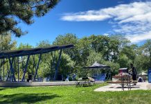Seattle Launches Next Phase of Be’er Sheva Park Renovations A large shelter provides rain protection over the stage alongside picnic table and playground equipment and a lawn with a row of trees in the background.