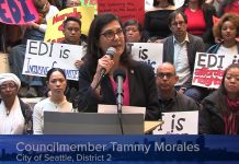 Rivera Walks Back Raid of Anti-Displacement Funds, Claims Critics Are Misinformed Morales speaks at a podium and several rows of supporters hold signs in support of the EDI program and against the budget raid.