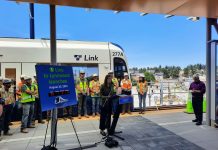 Sound Transit Begins Lynnwood Link Testing, Countdown Clock Mestas stands next to a countdown clock with construction workers lined up behind her in front of a Link train.