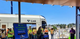 Mestas stands next to a countdown clock with construction workers lined up behind her in front of a Link train.