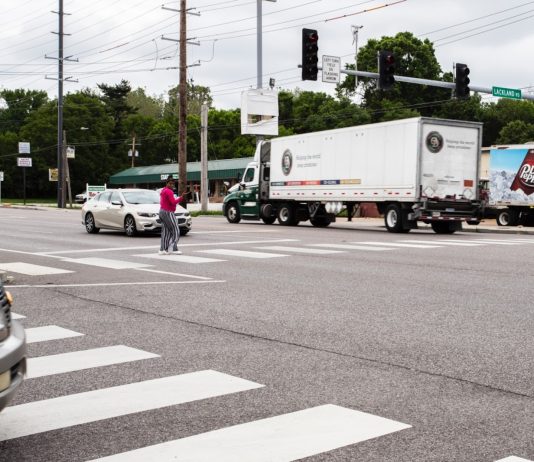 U.S. Pedestrian Deaths Rose to 40-Year High in 2022 A Black woman crosses in a crosswalk in a very wide busy road as a semi truck zooms by.