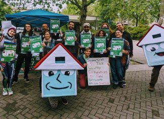 Seattle Social Housing Staffs Up, Nets $115 Million A group of about 20 advocates pose with signs next to House-y the social housing mascot