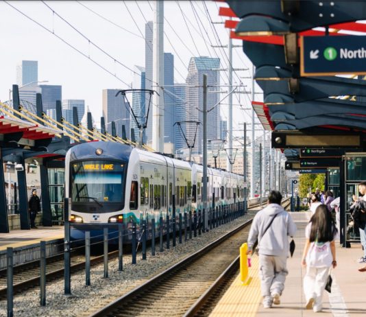 Sound Transit Launches Surveys To Plan South Seattle Link Infill Stations Two riders walked down the platform with the Seattle skyline in the distance.
