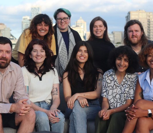 Apply to Join The Urbanist Election Committee The glass towers of the Seattle skyline peaks over the shoulders of the group.