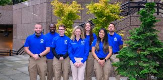 Seven CARE members wear logoed blue short sleeve shirts that are their official garb. These pose of the step of Seattle City Hall.
