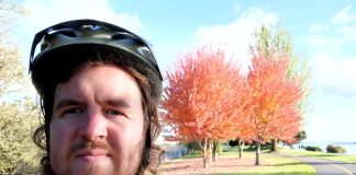 Ryan Packer in a bike helmet along a bike path with an autumn-colored tree behind