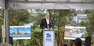 Habitat for Humanity Touts Its Largest Building Ever in Columbia City Groundbreaking Heck stands at a Habitat for Humanity Seattle-King County podium between two poster boards showing renderings of the future five-story building.