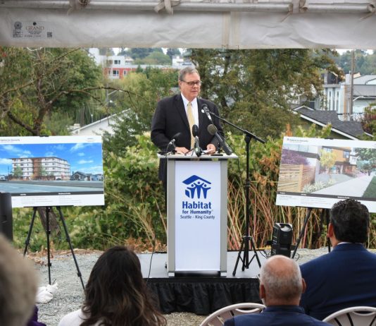 Habitat for Humanity Touts Its Largest Building Ever in Columbia City Groundbreaking Heck stands at a Habitat for Humanity Seattle-King County podium between two poster boards showing renderings of the future five-story building.