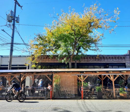 Policy Lab: Why Are Seattle Restaurants So Expensive? A pergola shelters a street cafe on Ballard Avenue, with a person biking by in the street.