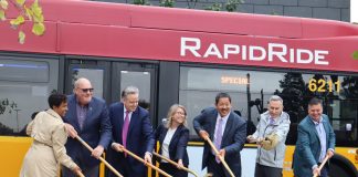 Officials stand in front of a red RapidRide bus with golden shovels with a scoop of ceremonial dirt.