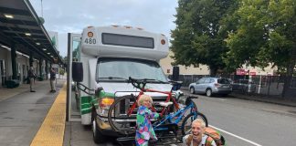 Op-Ed: Vote No on Initiative 2117 to Ensure Mobility for Washingtonians Anna Zivarts and her son smile and load a bike on the rack in front of a bus while it waits at a stop.