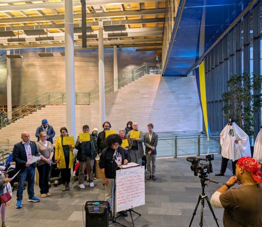 Seattle Rejects Capital Gains Proposal, but Progressive Tax Time Is Nigh Shemona Moreno is at the lectern with a dozen advocates holding signs in defense of JumpStart investments. Two advocates wear ghost costumes with cop hats representing the ghost cop positions that mayor and council prioritizes for funding.