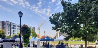 A central square in downtown Redmond has a row of bike parking and tents set up for a street far. Midrise apartment buildings ring the square and a construction crane adds another.