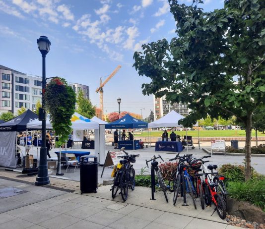 Redmond Greenlights Center Upzones, Sixplexes Citywide, Higher Affordability Requirements A central square in downtown Redmond has a row of bike parking and tents set up for a street far. Midrise apartment buildings ring the square and a construction crane adds another.